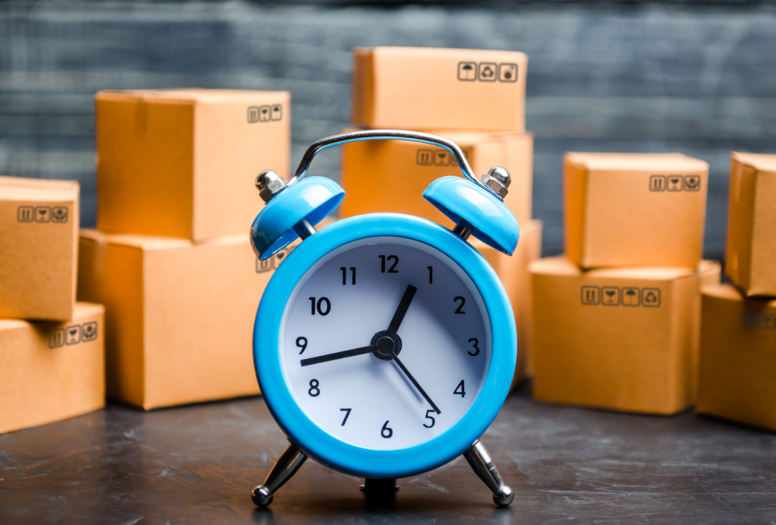 Cardboard boxes and a blue alarm clock. Time of delivery. Limited supply, shortage of goods in stock, hype and consumer fever. Time of delivery. concept of buying and selling goods.
